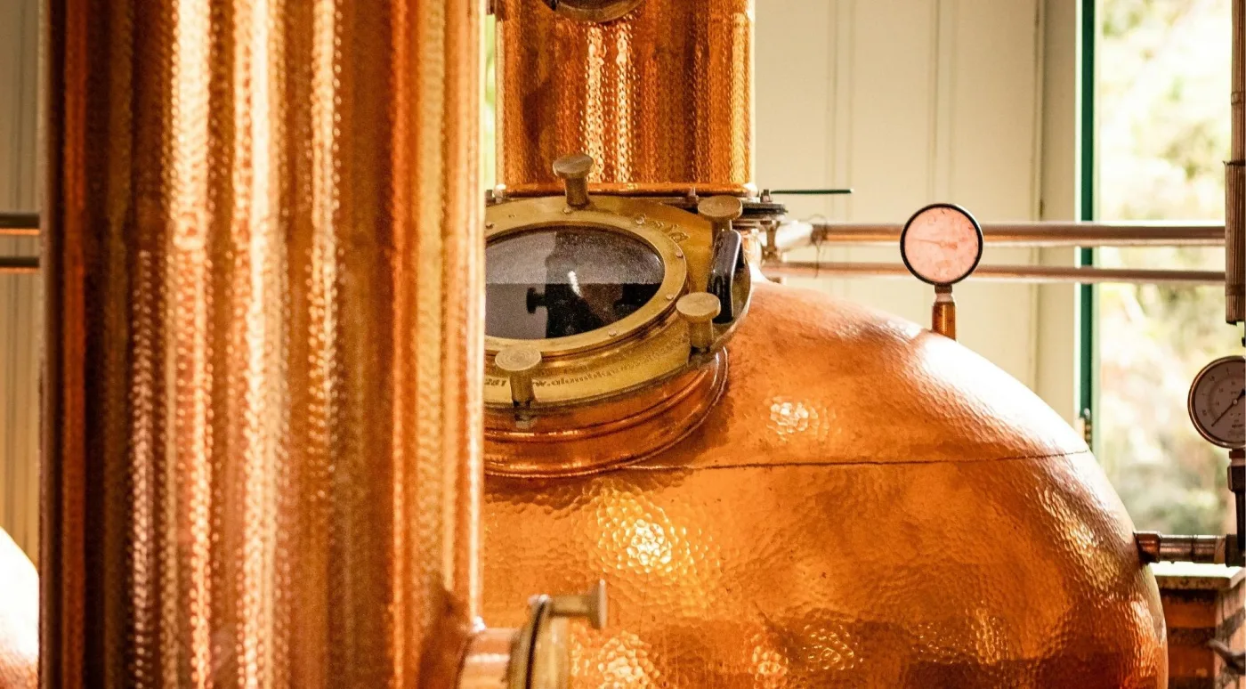 Close-up of a gleaming copper pot still with its brass spirit-safe window