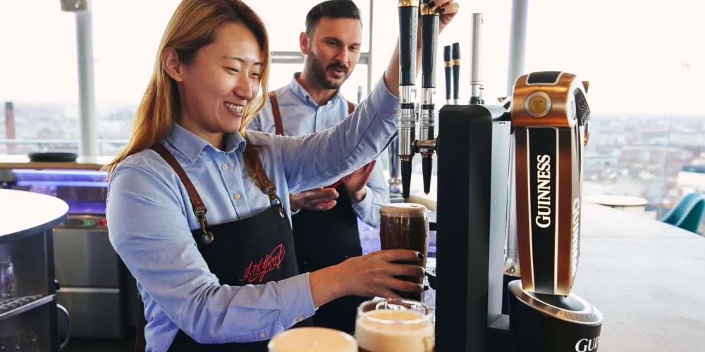 A bartender pouring a fresh pint of Guinness in the Gravity Bar above the Dublin skyline